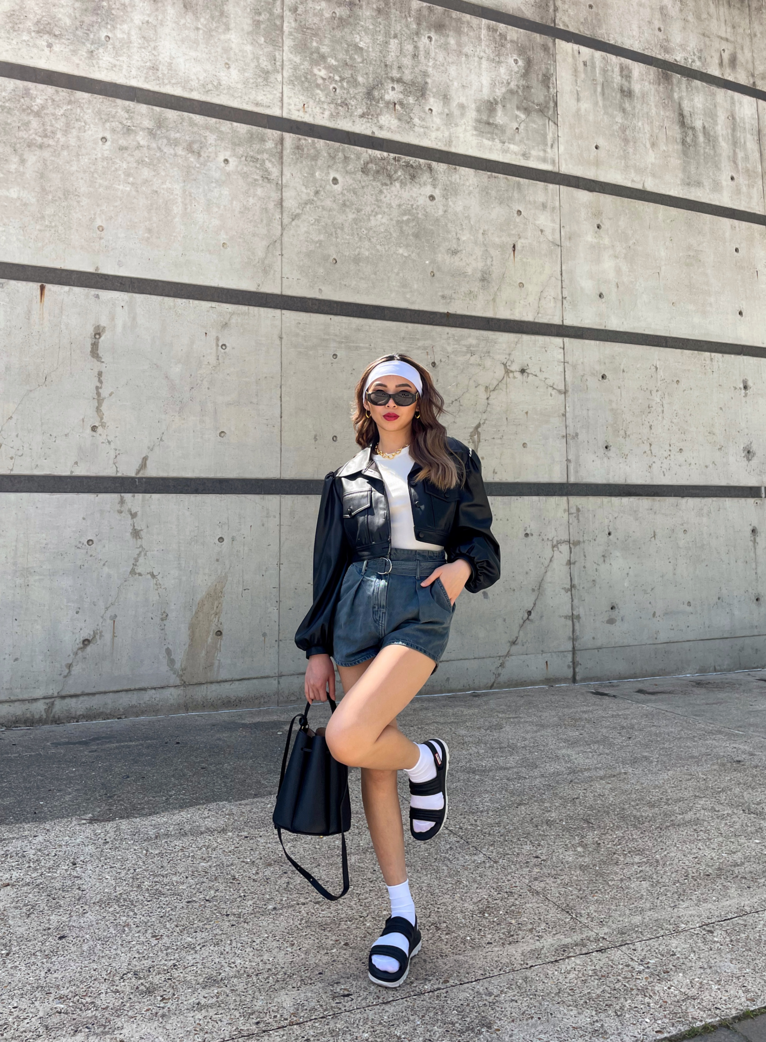 A trendy micro-influencer from the fashion industry, wearing a black jacket and shorts, striking a pose in front of a wall.