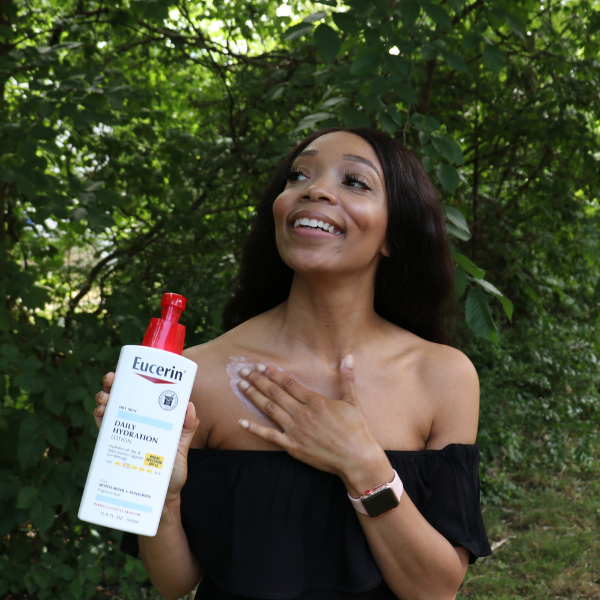 African-american woman smiling and holding and Eucerin lotion bottle, advocating for healthy skin.