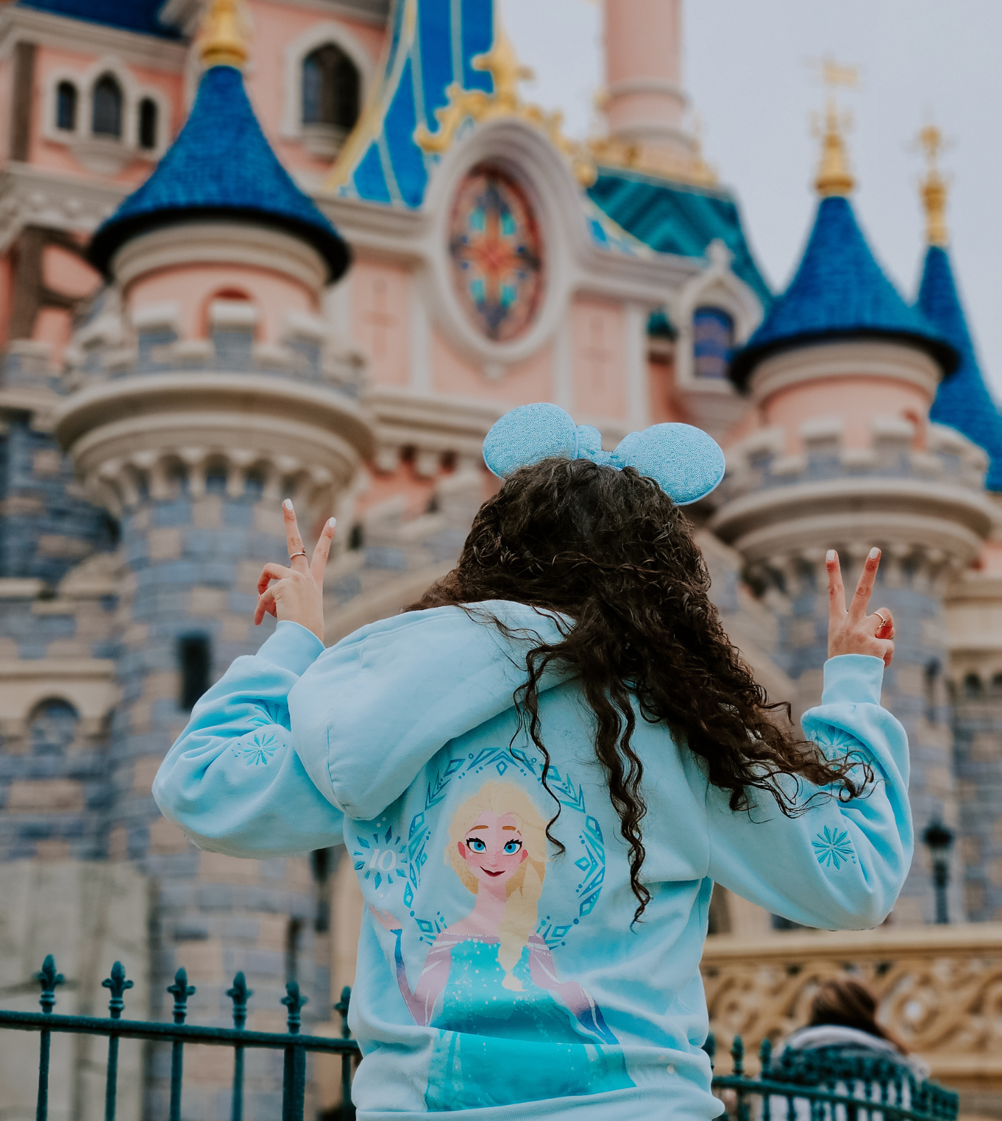 A girl in a Frozen hoodie standing in front of a Disney castle, creating magical memories.