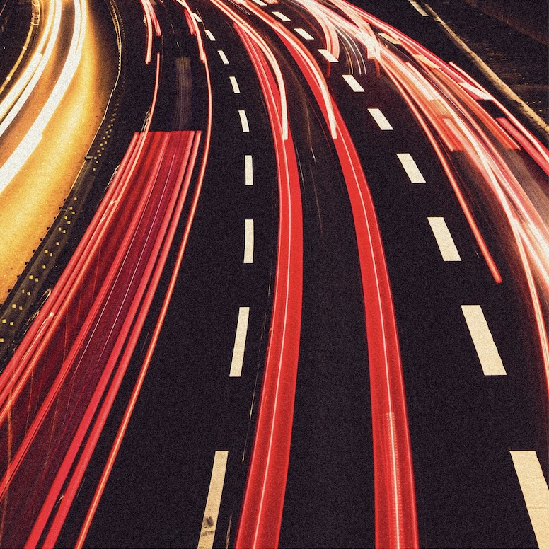 Long-exposure aerial shot of highway traffic light trails at night, representing creative velocity and content at scale